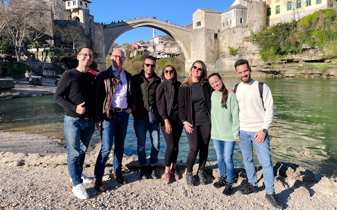 Group of tourists by the Neretva River with Mostar Bridge in Bosnia in the background.