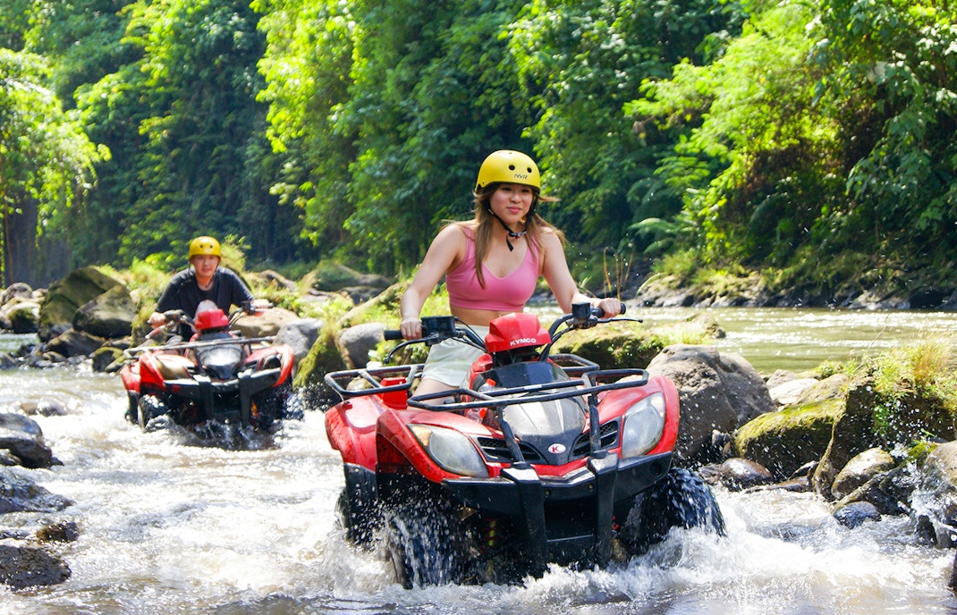 ATV riders crossing a river in Bali jungle during guided tour.