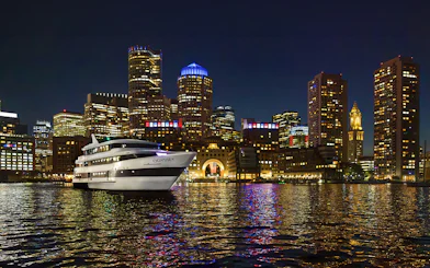 Premier Dinner Cruise ship on Boston Harbor with city skyline at night.