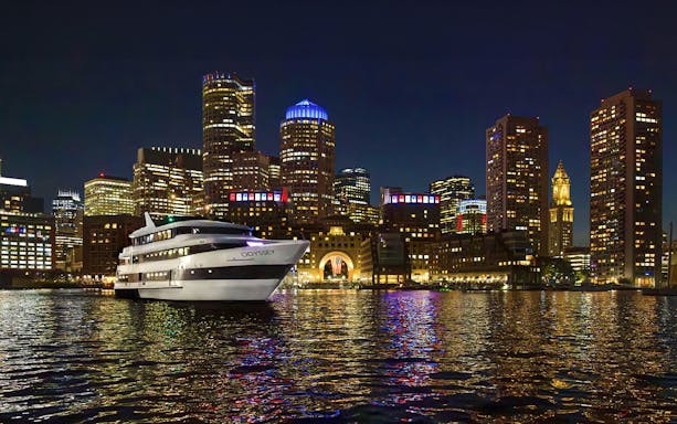 Premier Dinner Cruise ship on Boston Harbor with city skyline at night.