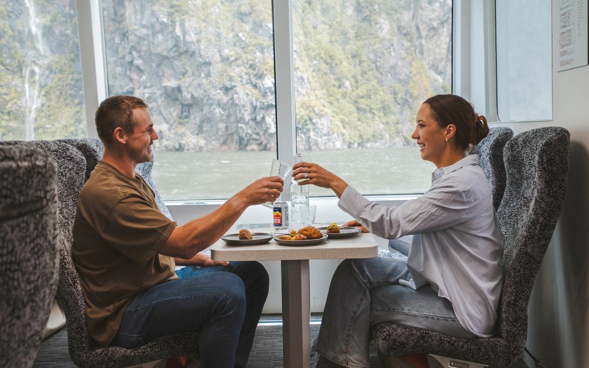 Couple enjoying a meal on Milford Sound nature cruise with scenic fjord view.