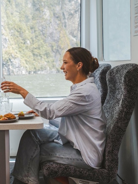 Couple enjoying a meal on Milford Sound nature cruise with scenic fjord view.