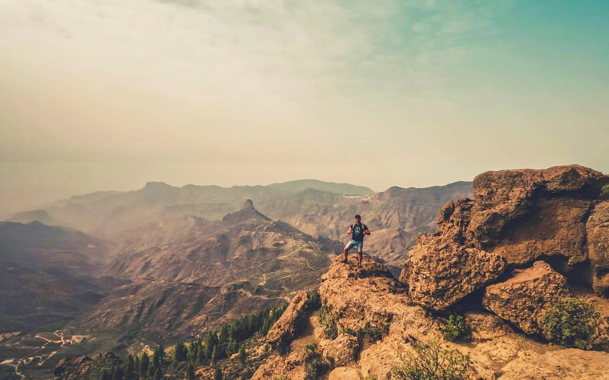 Hiker on rocky cliff with volcanic landscape in Gran Canaria.