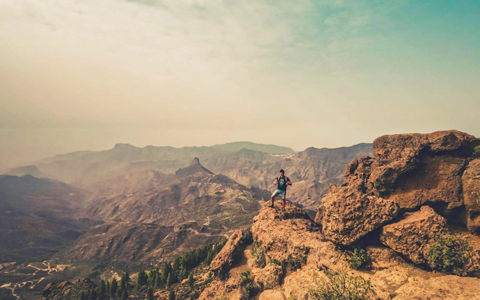 Hiker on rocky cliff with volcanic landscape in Gran Canaria.