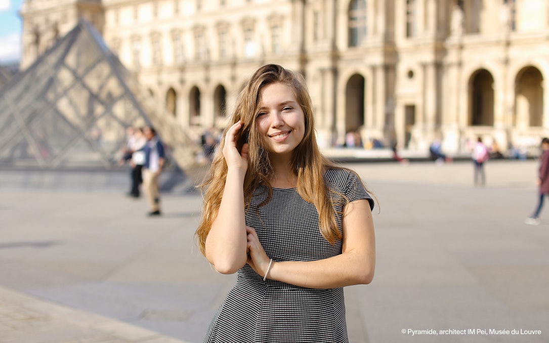 Person posing in front of the Louvre Pyramid, Paris during a professional photoshoot.