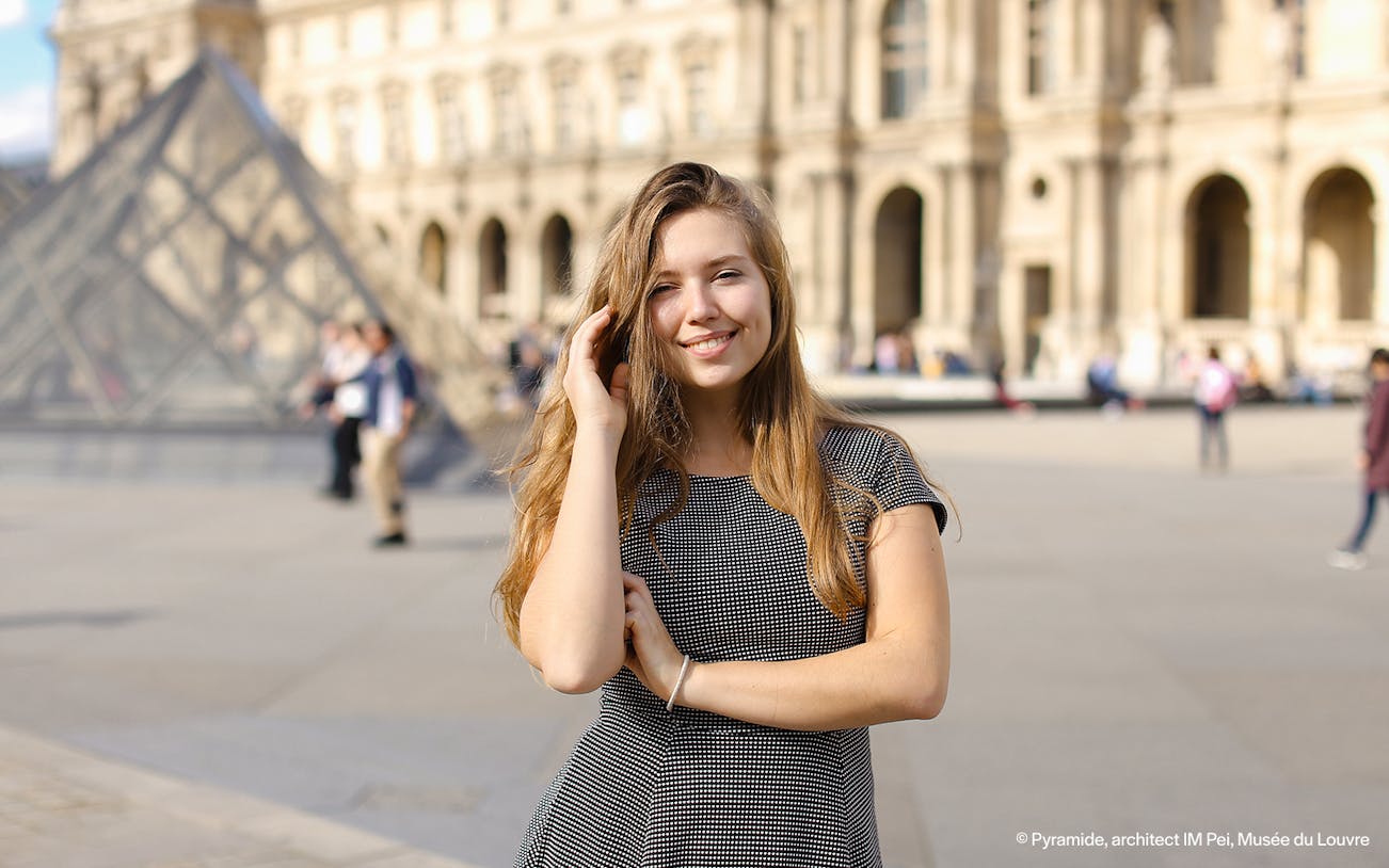 Person posing in front of the Louvre Pyramid, Paris during a professional photoshoot.