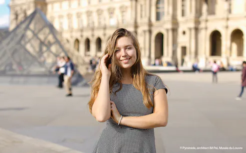 Person posing in front of the Louvre Pyramid, Paris during a professional photoshoot.