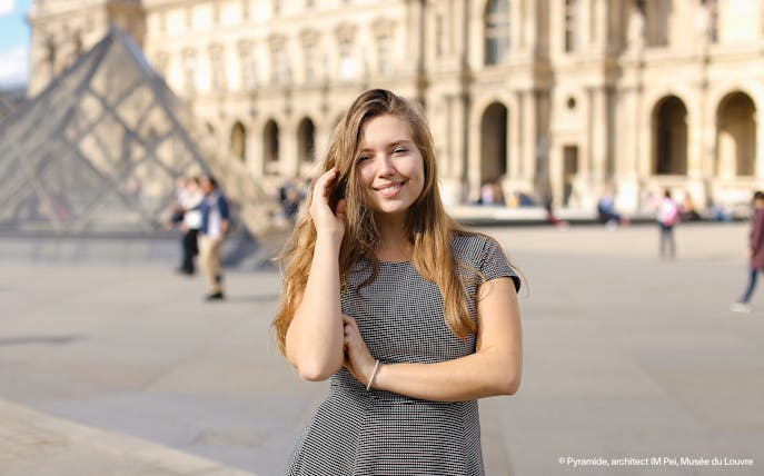 Person posing in front of the Louvre Pyramid, Paris during a professional photoshoot.