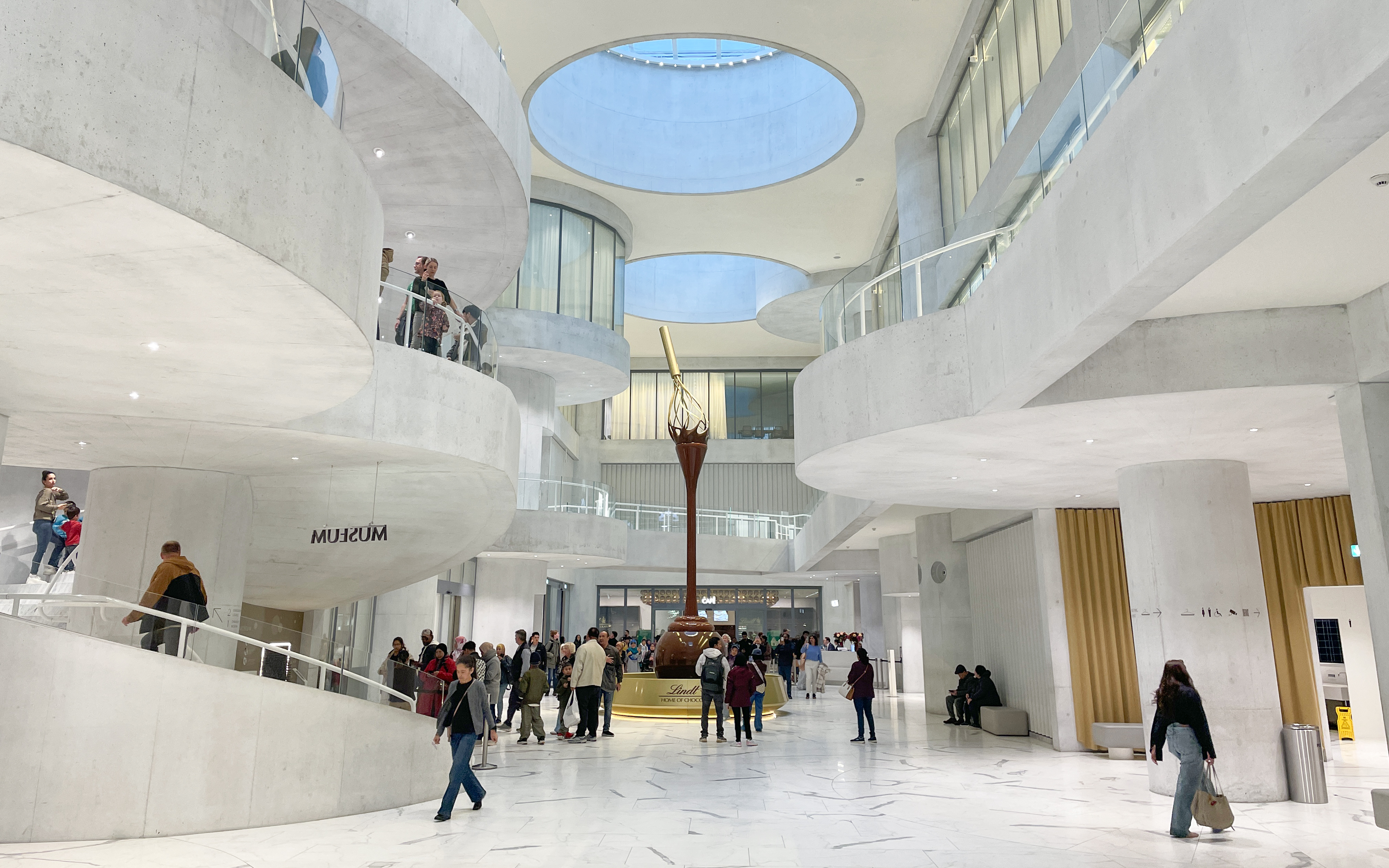 Visitors inside Lindt Home of Chocolate Museum Zurich, featuring modern architecture and a large chocolate fountain.