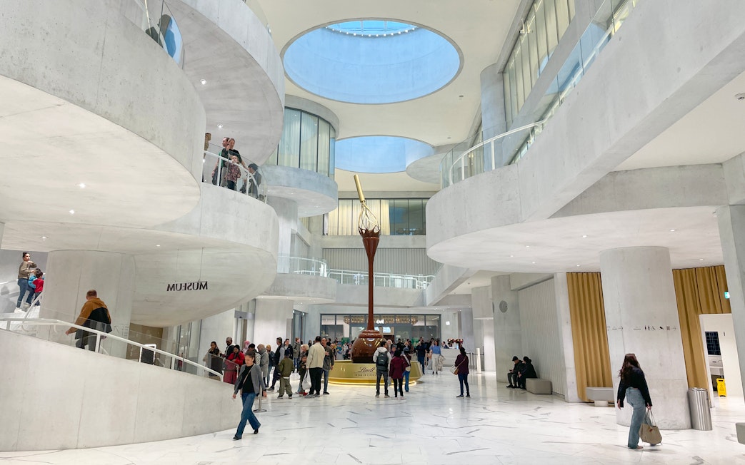 Visitors inside Lindt Home of Chocolate Museum Zurich, featuring modern architecture and a large chocolate fountain.