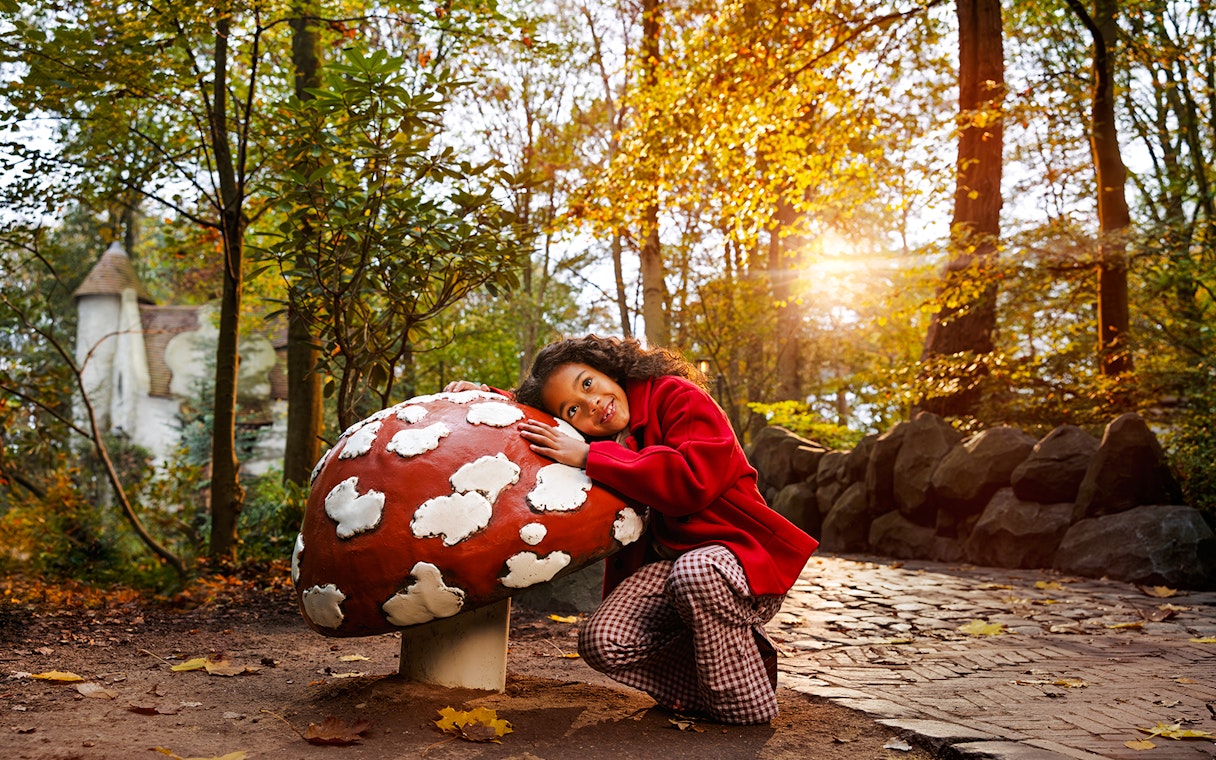 Child smiling next to a large mushroom sculpture at Efteling Theme Park.