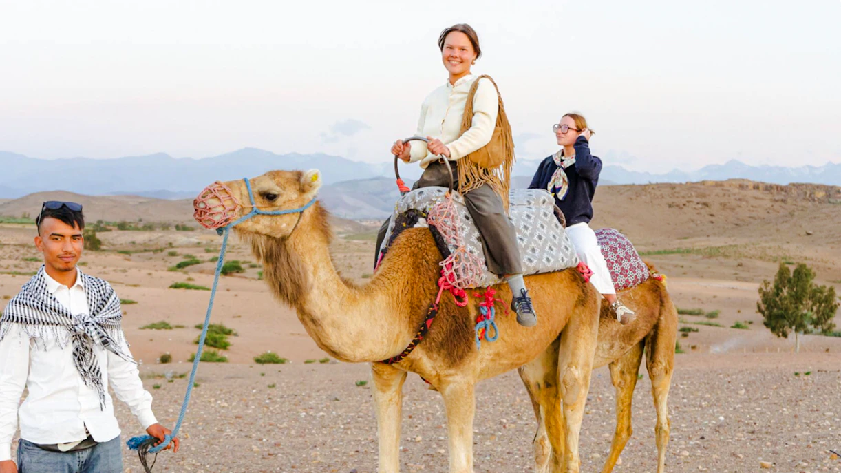 Person riding camel in Agafay Desert, Marrakesh with guide leading.