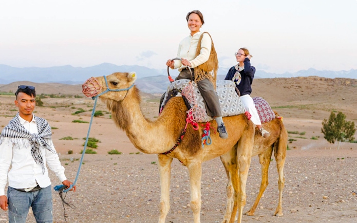 Person riding camel in Agafay Desert, Marrakesh with guide leading.