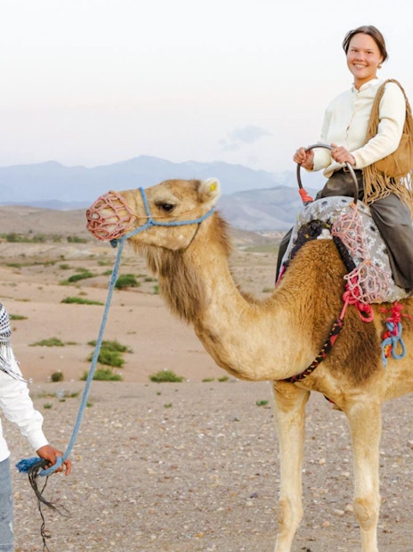 Person riding camel in Agafay Desert, Marrakesh with guide leading.