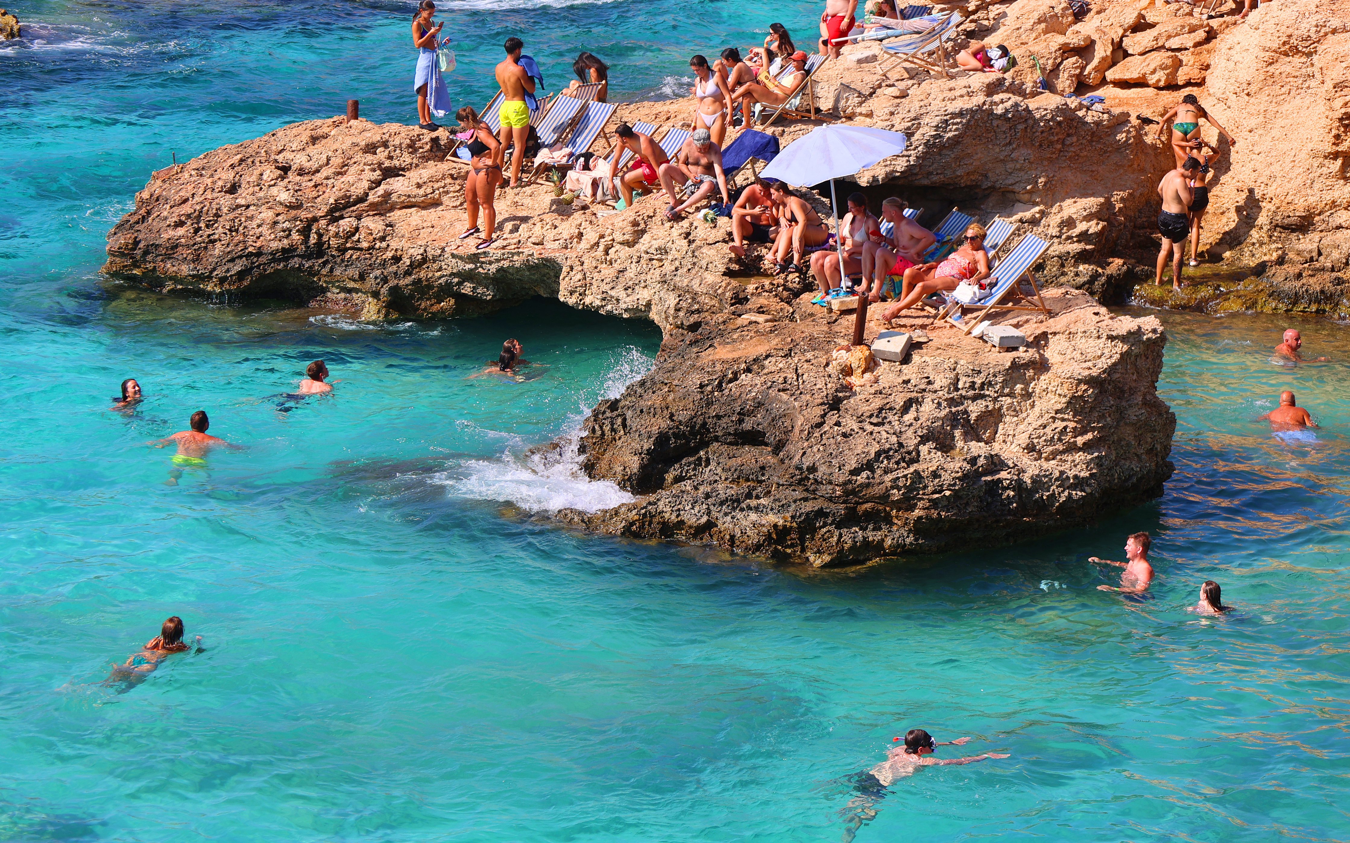 People swimming and relaxing on rocky shore at Blue Lagoon, Malta.