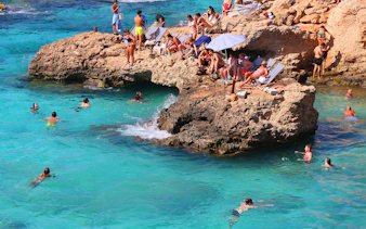 People swimming and relaxing on rocky shore at Blue Lagoon, Malta.