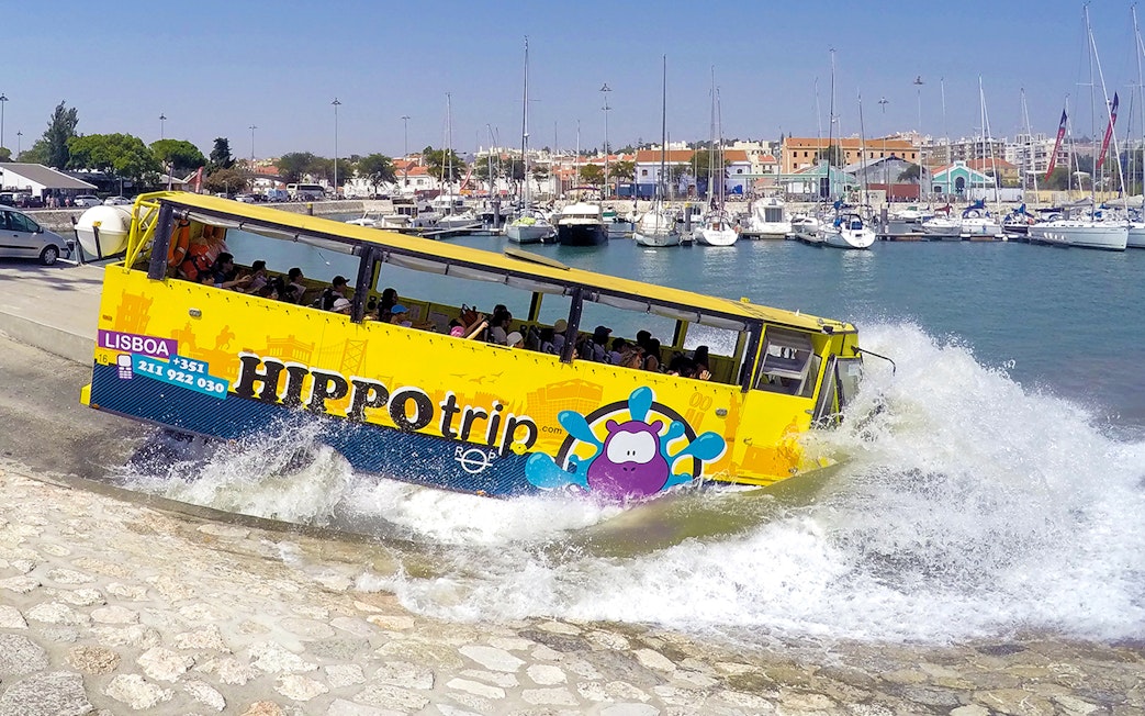 Amphibious tour bus entering water in Lisbon marina during sightseeing tour.