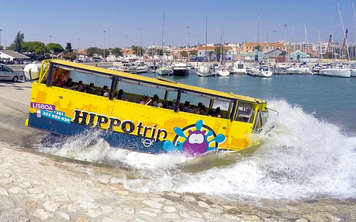 Amphibious tour bus entering water in Lisbon marina during sightseeing tour.