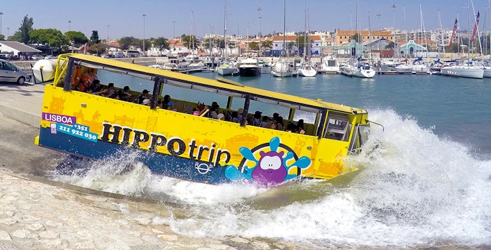 Amphibious tour bus entering water in Lisbon marina during sightseeing tour.
