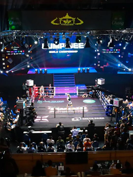 Muay Thai fighters in a match at One Lumpinee Stadium with audience and stage lights.