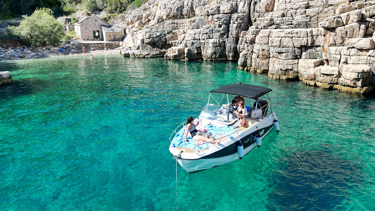 Speedboat with tourists on clear waters near rocky shore, North Shore of Hvar Island.