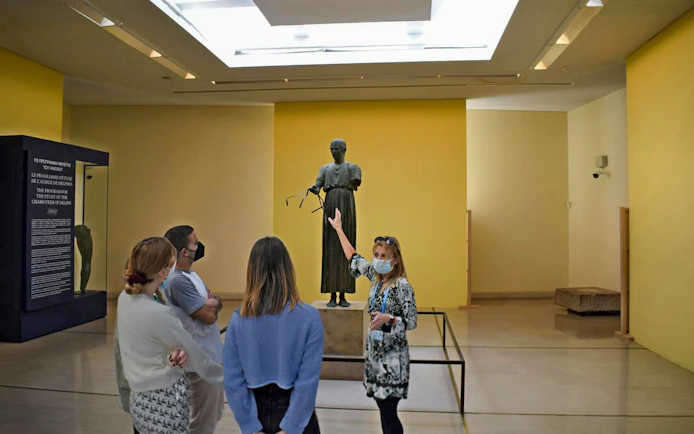 Visitors viewing the Charioteer of Delphi statue at Delphi Archaeological Museum, Greece.