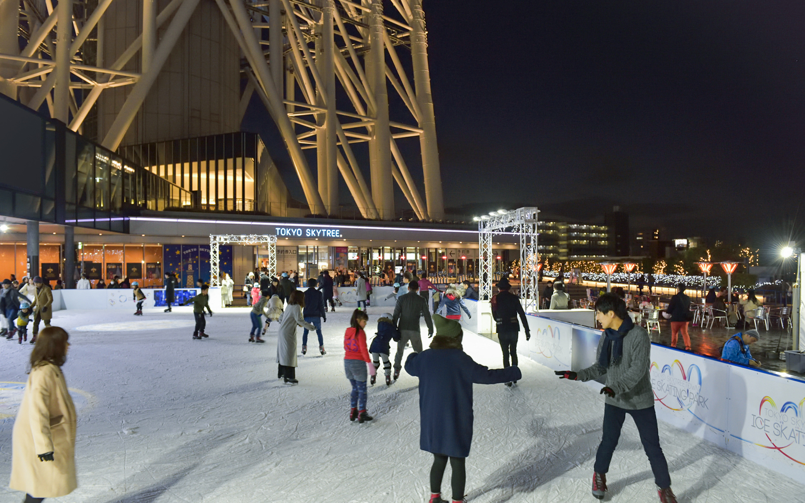 People ice skating at night near Tokyo Skytree, illuminated with festive lights.