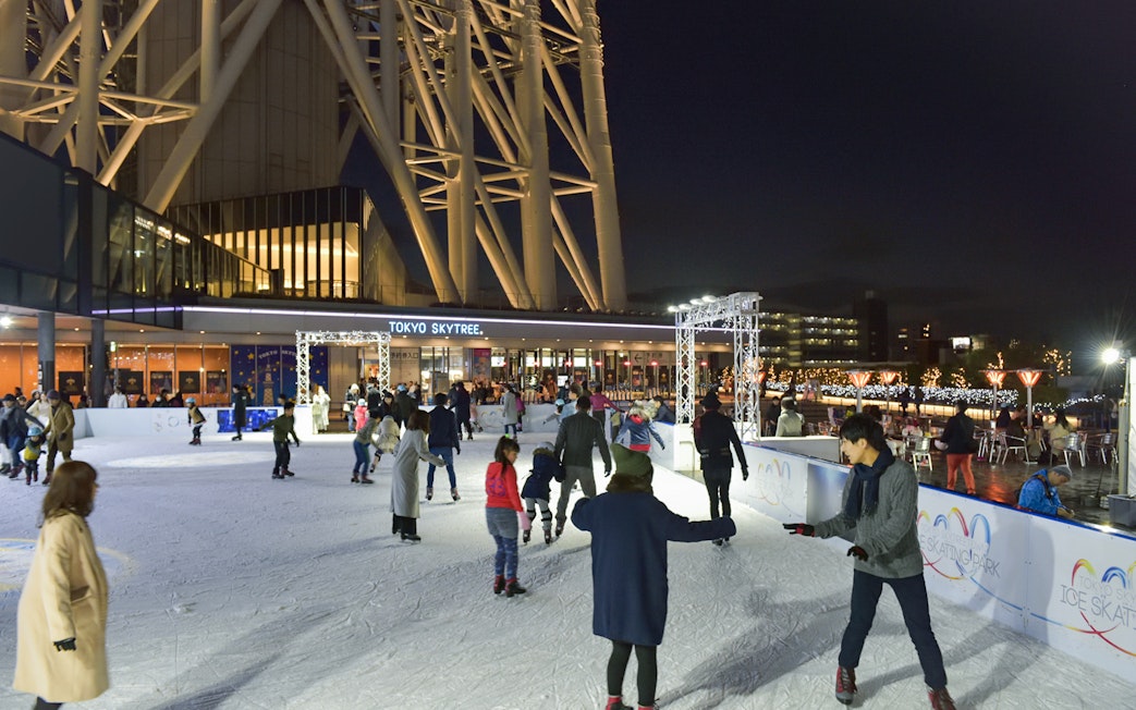People ice skating at night near Tokyo Skytree, illuminated with festive lights.