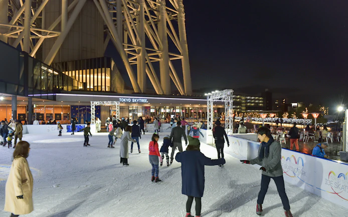 People ice skating at night near Tokyo Skytree, illuminated with festive lights.