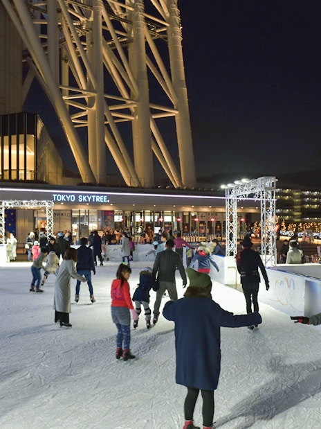 People ice skating at night near Tokyo Skytree, illuminated with festive lights.