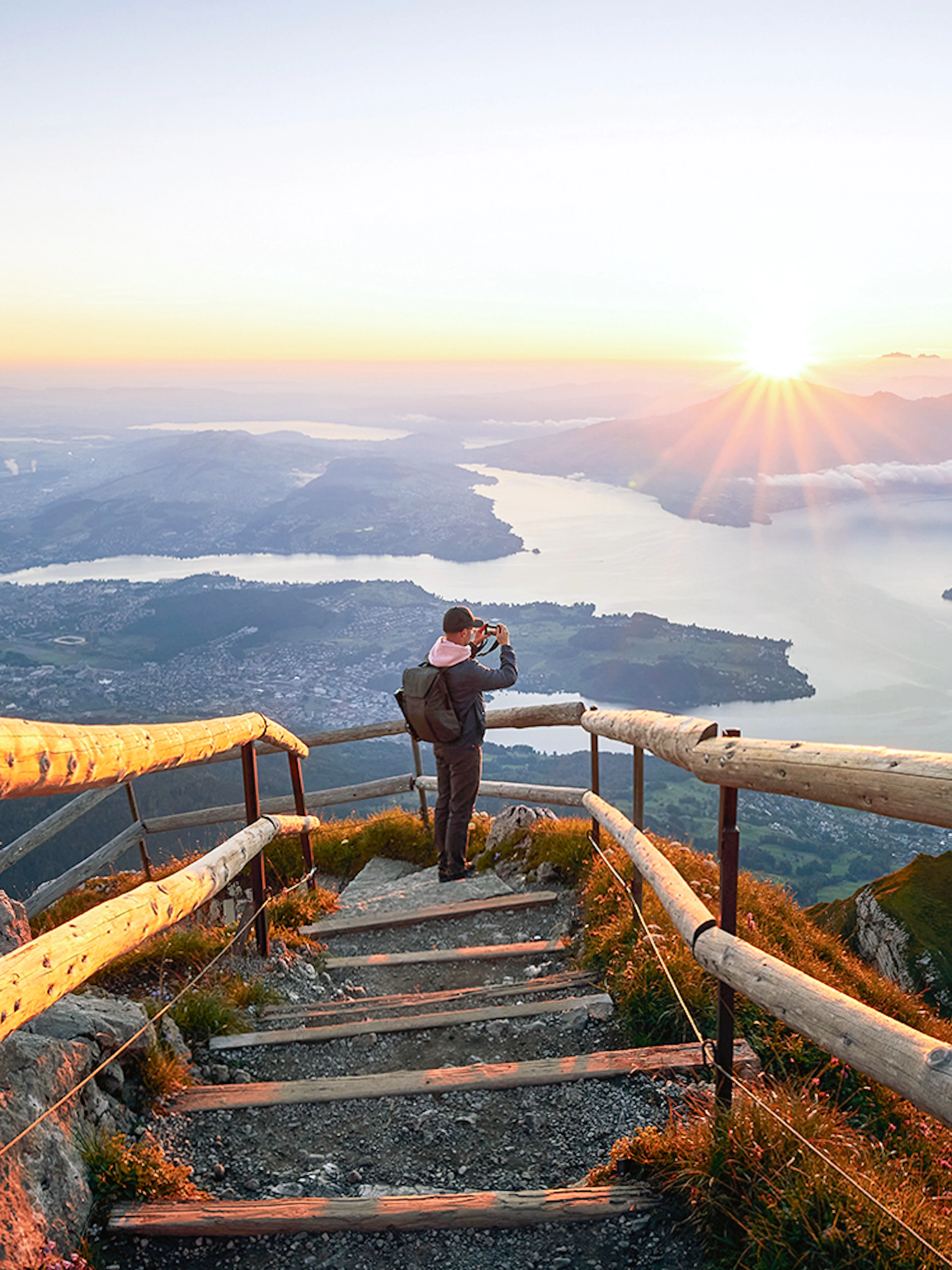 Man photographing sunrise over Lake Lucerne from Mount Pilatus summit.