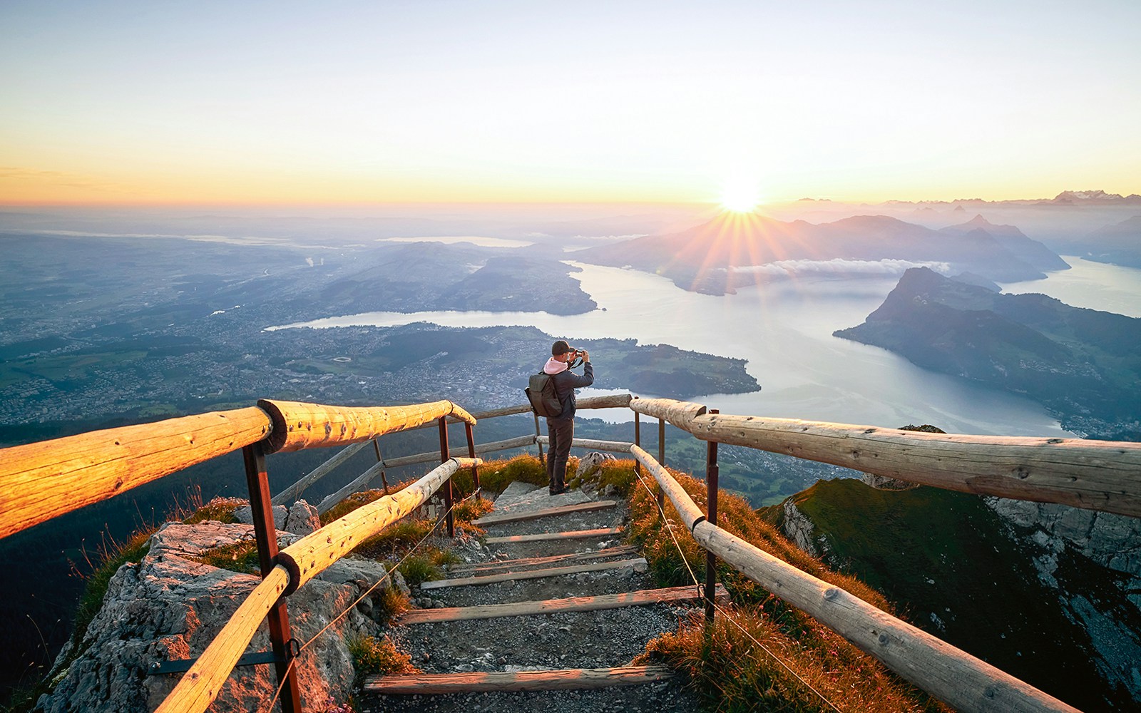 Man photographing sunrise over Lake Lucerne from Mount Pilatus summit.