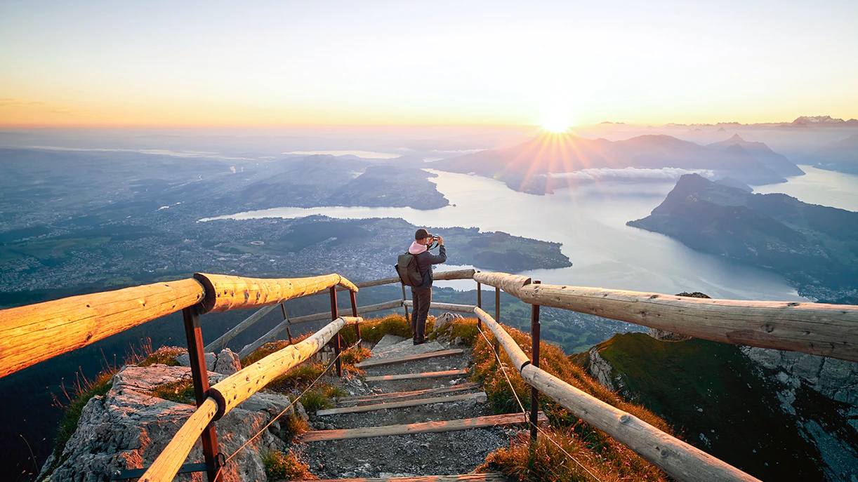 Man photographing sunrise over Lake Lucerne from Mount Pilatus summit.