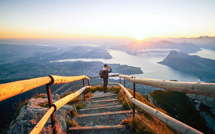 Man photographing sunrise over Lake Lucerne from Mount Pilatus summit.