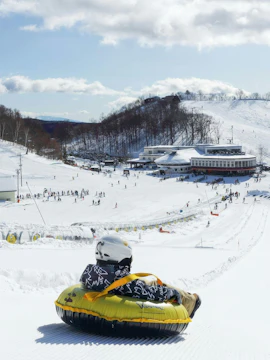 Person tubing down snowy slope at Hakuba Kashimayari Ski Resort, Japan.