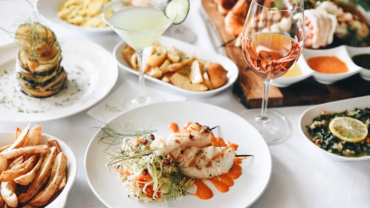 Mediterranean lunch with grilled fish skewers, vegetable stack, and wine.