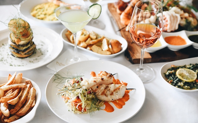 Mediterranean lunch with grilled fish skewers, vegetable stack, and wine.