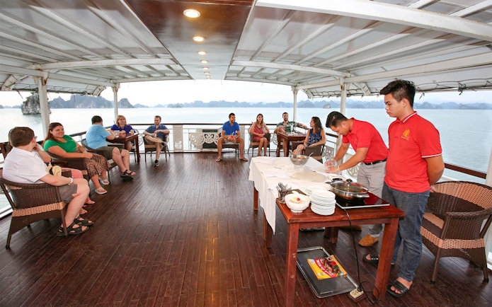 Guests relaxing on a Halong Bay 3-star cruise deck with staff preparing a meal.