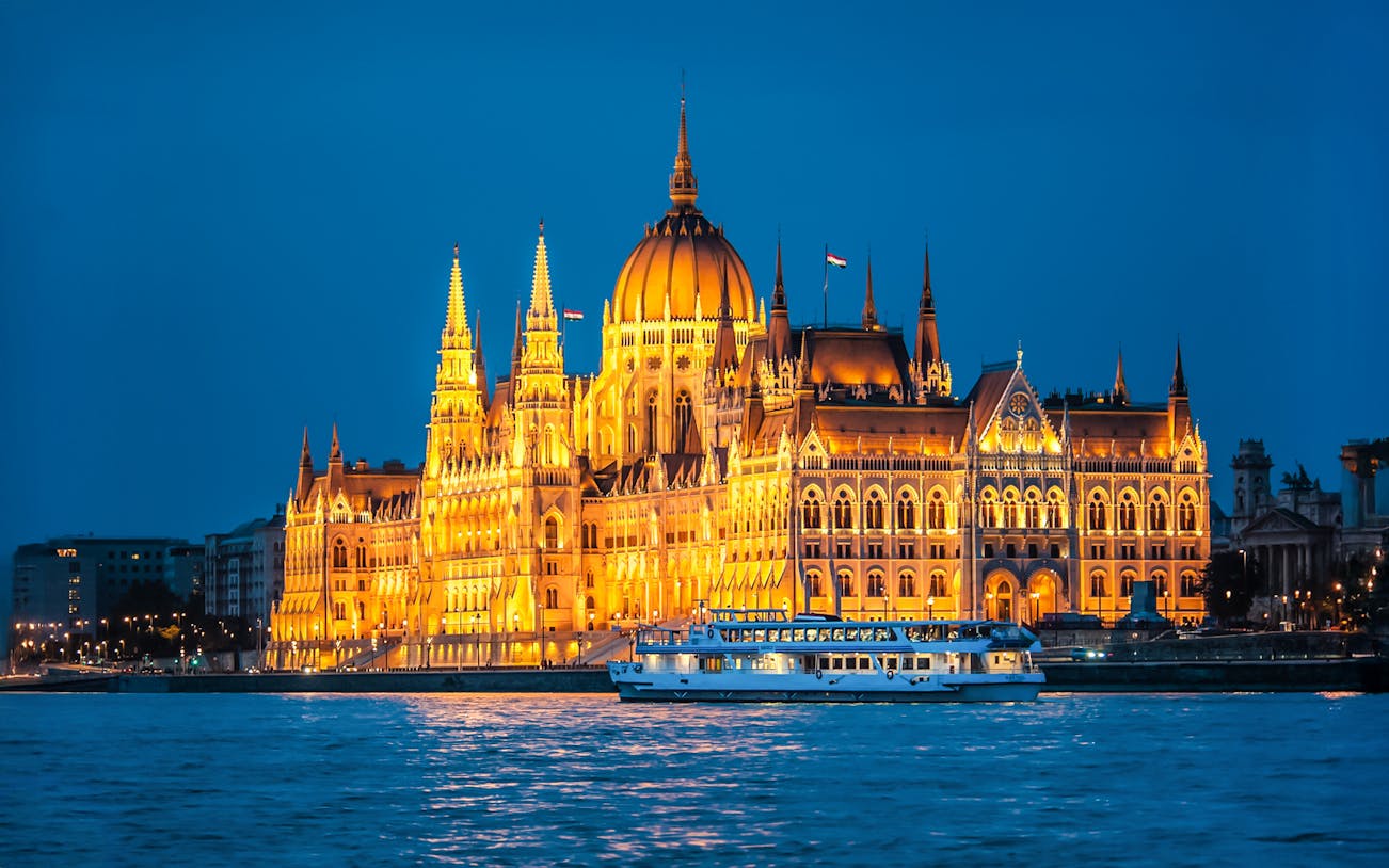 Parliament building illuminated at night with a sightseeing cruise on the river.