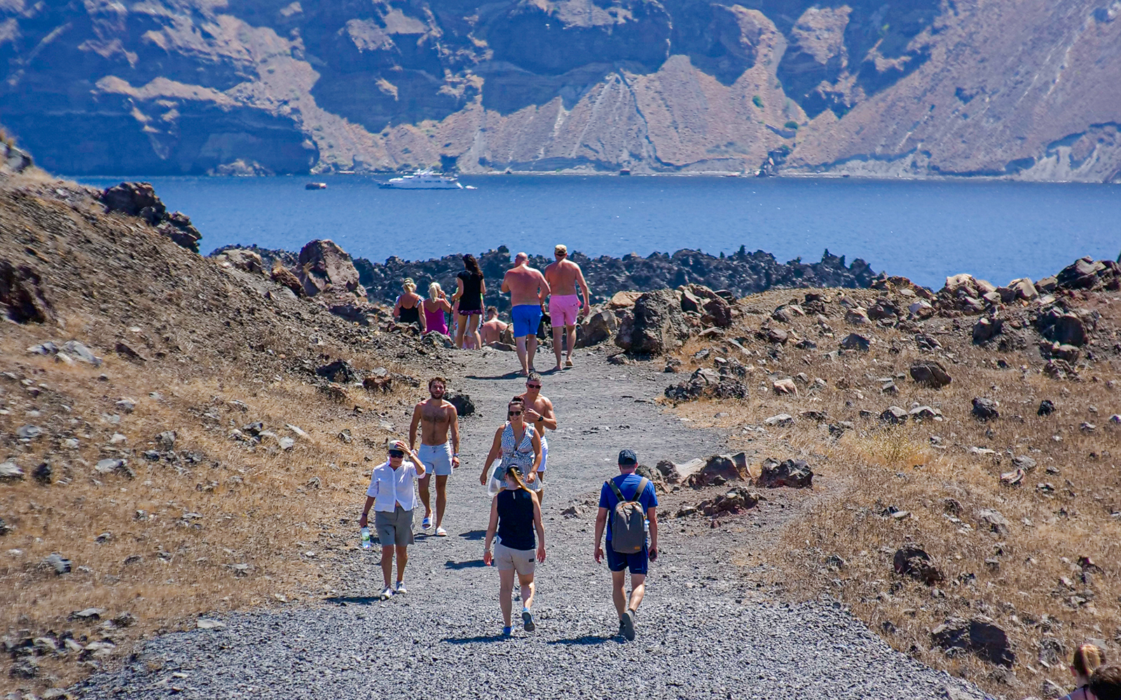 Guests hiking on a rocky path during Santorini volcanic cruise tour with sea view.