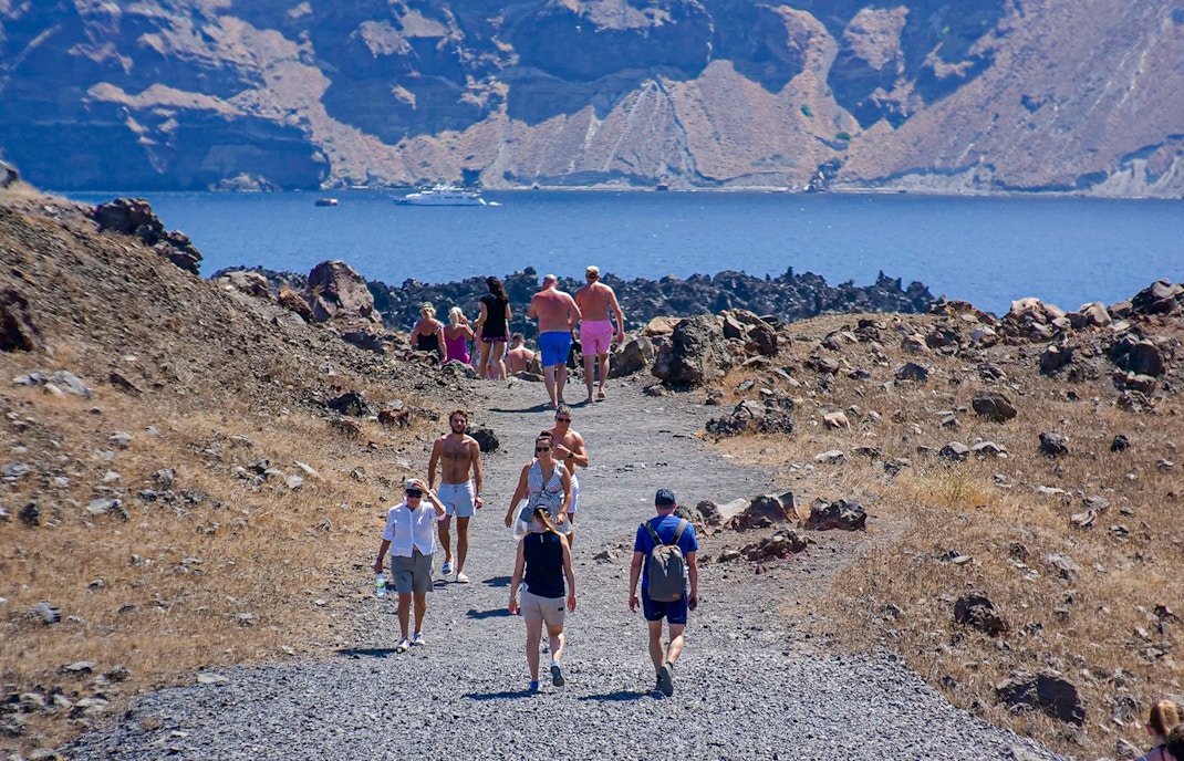 Guests hiking on volcanic terrain during Santorini cruise tour, Greece.