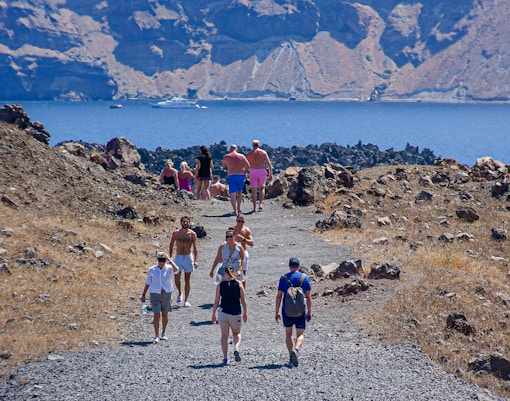 Guests hiking on a rocky path during Santorini volcanic cruise tour with sea view.