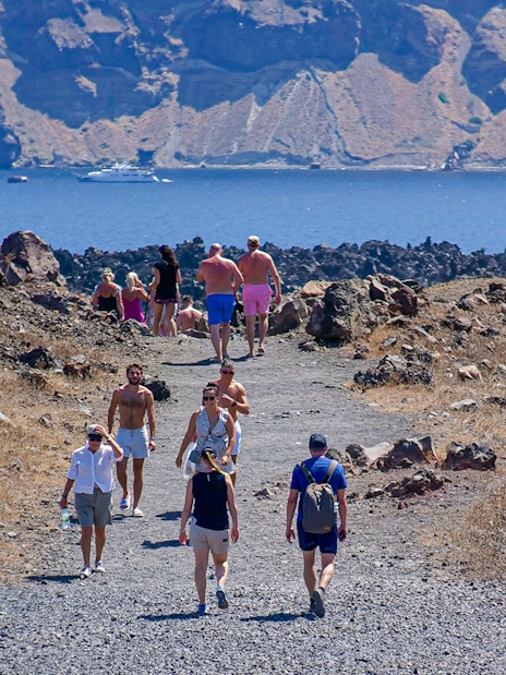 Guests hiking on a rocky path during Santorini volcanic cruise tour with sea view.