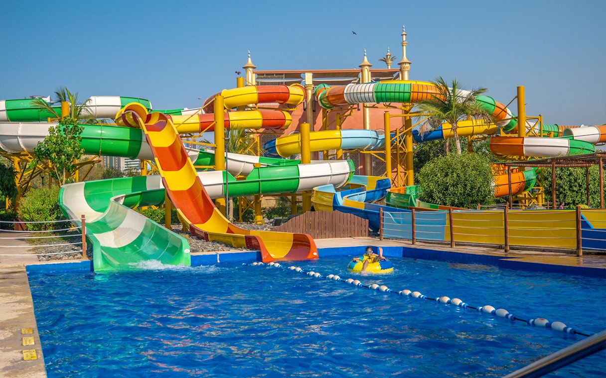 Colorful water slides at Al Montazah Water Park with a child on a yellow float in the pool.