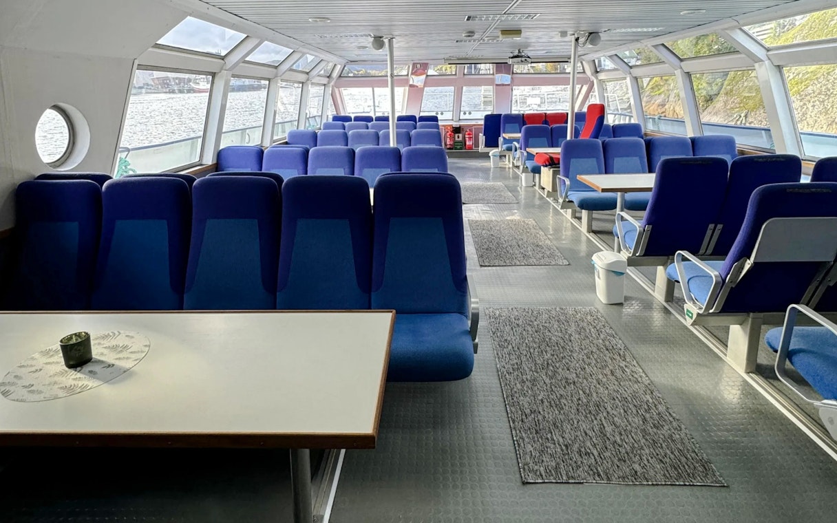 Interior seating area of a Trollfjord cruise ship, Lofoten, with large windows and blue seats.