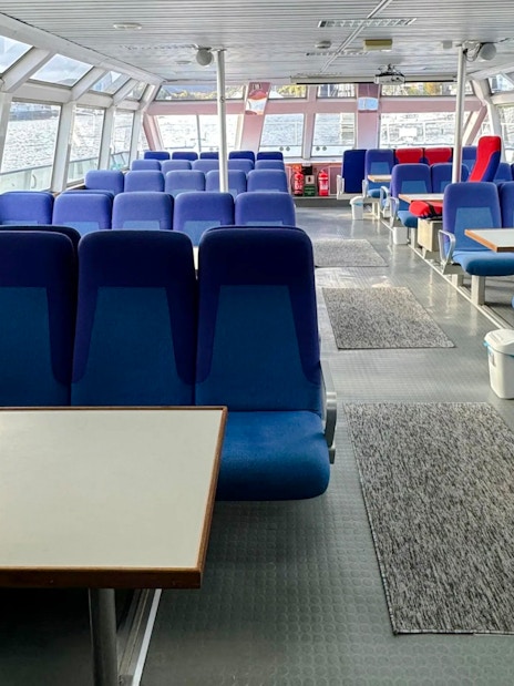Interior seating area of a Trollfjord cruise ship, Lofoten, with large windows and blue seats.