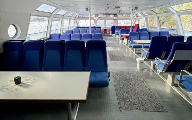 Interior seating area of a Trollfjord cruise ship, Lofoten, with large windows and blue seats.