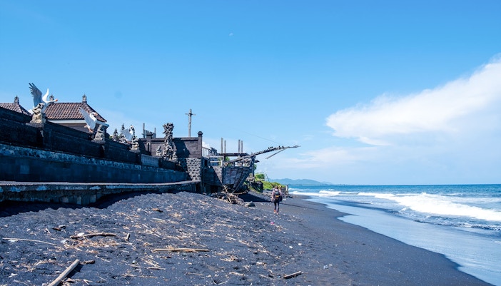 Kusamba Harbor black sand beach with traditional Balinese architecture and ocean view.