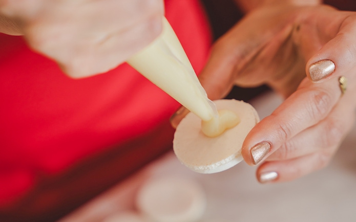 Piping cream onto a macaron shell during a Paris macaron-making workshop.