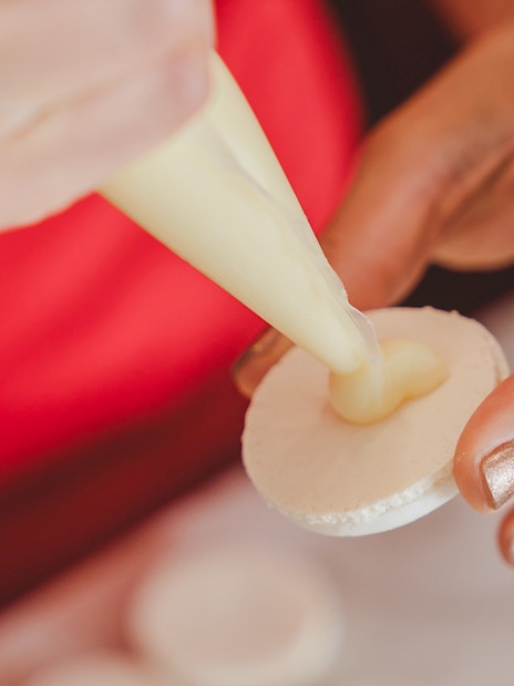 Piping cream onto a macaron shell during a Paris macaron-making workshop.